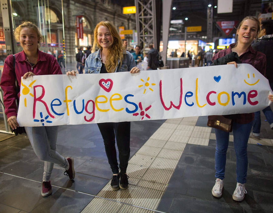 girls-standing-with-sign-welcoming-migrants-70132